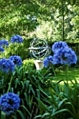 DAVID HARBER SUNDIALS: ARMILLARY SPHERE SUNDIAL ON STONE PLINTH WITH AGAPANTHUS IN FOREGROUND