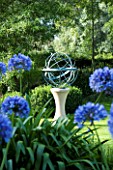 DAVID HARBER SUNDIALS: BRONZE ARMILLARY SPHERE SUNDIAL ON STONE PLINTH IN COTTAGE GARDEN WITH AGAPANTHUS