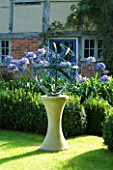DAVID HARBER SUNDIALS: BRONZE ARMILLARY SPHERE SUNDIAL ON STONE PLINTH IN COTTAGE GARDEN WITH BLUE AGAPANTHUS