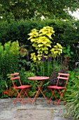 WILKINS PLECK  STAFFORDSHIRE: HOT GARDEN: A PLACE TO SIT - PATIO WITH RED TABLE AND CHAIRS WITH CATALPA BIGNOIDES AUREA