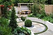 SMALL LOW MAINTENANCE GARDEN IN LONDON DESIGNED BY CHARLOTTE ROWE. RAISED CONCRETE BEDS  BOX BALLS IN PAVING  WOODEN PERGOLA  TABLE AND CHAIRS