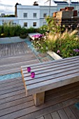ROOF GARDEN  HOLLAND PARK  LONDON. DESIGNER: CHARLOTTE ROWE. WOODEN BENCH WITH VOTIVE CANDLES IN MAUVE GLASS HOLDER ON IPE DECKED TERRACE WITH BLUE GLASS GRAVEL