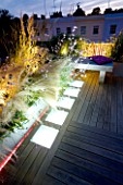 ROOF GARDEN  HOLLAND PARK  LONDON. DESIGNER: CHARLOTTE ROWE. DECKED TERRACE AT NIGHT WITH LED LIGHTING AND BLUE GLASS GRAVEL  STIPA TENUISSIMA  GAURA LINDHEIMERI