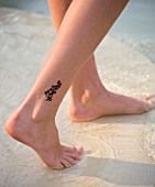 GIRL WITH TATTOO ON LEG WALKING IN A SHALLOW POOL