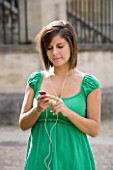 TEENAGE GIRL (16-17 YEARS) IN JEAN MINISKIRT AND GREEN TOP LISTENING TO MP3 PLAYER. TEENAGE GIRLS  ONE TEENAGE GIRL ONLY  IPOD  MUSIC  CASUAL CLOTHING  WAIST UP