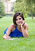 TEENAGE GIRL (16-17 YEARS) IN BLUE TOP LYING ON GRASS WRITING. SMILING  TEENAGE GIRLS  ONE TEENAGE GIRL ONLY  CASUAL CLOTHING  HAPPY  HAPPINESS  STUDENT  COLLEGE  IN THE PARK