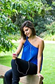 TEENAGE GIRL (16-17 YEARS) IN BLUE TOP SITTING ON PARK BENCH LISTENING TO MP3 PLAYER. MUSIC  TEENAGE GIRLS  ONE TEENAGE GIRL ONLY  CASUAL CLOTHING  STUDENT  COLLEGE  MUSIC