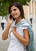 TEENAGE GIRL (16-17 YEARS) IN WHITE SHIRT AND BLACK TROUSERS TALKING ON MOBILE PHONE  BAG OVER SHOULDER. TEENAGE GIRLS  ONE TEENAGE GIRL ONLY  STUDENT  COLLEGE  CASUAL CLOTHING
