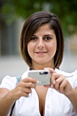 TEENAGE GIRL (16-17 YEARS) IN WHITE SHIRT TAKING A PHOTOGRAPH. BAG OVER SHOULDER. TEENAGE GIRLS  ONE TEENAGE GIRL ONLY  STUDENT  COLLEGE  CASUAL CLOTHING  PHOTOGRAPH  PHOTOGRAPHY