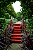 THROUGHAM COURT  GLOUCESTERSHIRE. DESIGNER: CHRISTINE FACER: THE ROYAL STEPS - RED CARPET UP STEPS WITH PHORMIUMS AND PLEACHED LIME WALK BEYOND