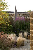RICKYARD BARN GARDEN  NORTHAMPTONSHIRE - VIEW THROUGH STONE WALL INTO GRAVEL GARDEN IN SEPTEMBER WITH STIPA TENUISSIMA  AND DRIFTWOOD SCULPTURE