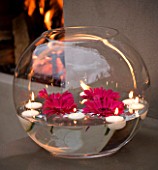 DESIGNER - CHARLOTTE ROWE  LONDON: CHARLOTTE ROWES OWN GARDEN AT NIGHT -  LARGE GLASS FISH BOWL FILLED WITH WATER WITH FLOATING CANDLES AND PINK GERBERAS