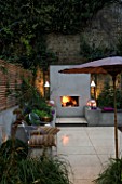 DESIGNER CHARLOTTE ROWE  LONDON: CHARLOTTE ROWES OWN GARDEN AT NIGHT - PORTUGUESE HONED LIMESTONE FLOORING  RENDERED RAISED BEDS AND FIREPLACE  PHILIPPE STARCK CHAIRS WITH CUSHION