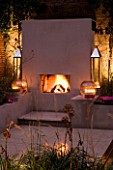DESIGNER - CHARLOTTE ROWE  LONDON: CHARLOTTE ROWES OWN GARDEN AT NIGHT - PORTUGUESE HONED LIMESTONE FLOORING  RENDERED RAISED BEDS  OUTDOOR FIREPLACE  GLASS BOWLS WITH CANDLES