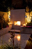 DESIGNER CHARLOTTE ROWE  LONDON: CHARLOTTE ROWES OWN GARDEN AT NIGHT - PORTUGUESE HONED LIMESTONE FLOORING  RENDERED RAISED BEDS  FIREPLACE AND TRELLIS