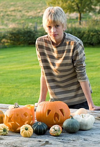 HALLOWEEN_BOY_AGED_13_ADMIRES_A_STILL_LIFE_ON_OUTDOOR_WOODEN_TABLE_WITH_PUMPKINS__SQUASHES_AND_GOUR
