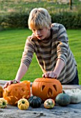 HALLOWEEN: BOY (AGED 13) ADMIRES A STILL LIFE ON OUTDOOR WOODEN TABLE WITH PUMPKINS  SQUASHES AND GOUR