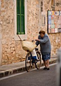 SUITE.DO. OLD WOMAN WALKING ALONG THE STREETS WITH A BICYCLE. SANTANYI  MALLORCA  SPAIN