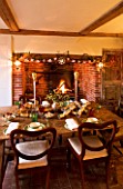 BOONSHILL FARM AT CHRISTMAS: THE DINING ROOM - TABLE LAID OUT FOR CHRISTMAS WITH CRACKERS  MISTLETOE IN SILVER CONTAINER AND FIRE. DESIGNER: LISETTE PLEASANCE