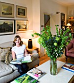 CHARLOTTE ROWES HOUSE - INTERIOR SHOT OF LIVING ROOM WITH TABLE WITH GREEN FLORAL DISPLAY AND CHARLOTTE READING BOOK