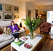 CHARLOTTE ROWES HOUSE - INTERIOR SHOT OF LIVING ROOM WITH TABLE WITH GREEN FLORAL DISPLAY AND CHARLOTTE READING BOOK