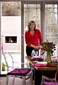 DESIGNER: CHARLOTTE ROWE  LONDON: CHARLOTTE IN THE DINING ROOM WITH THE GARDEN AND OUTDOOR FIREPLACE BEHIND