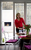 DESIGNER: CHARLOTTE ROWE  LONDON: CHARLOTTE IN THE DINING ROOM WITH THE GARDEN AND OUTDOOR FIREPLACE BEHIND