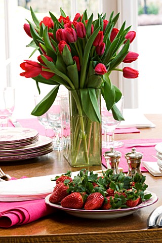 DESIGNER_CHARLOTTE_ROWE__LONDON_RED_TULIPS_IN_A_VASE_ON_THE_DINING_ROOM_TABLE_AND_FRESH_STRAWBERRIES