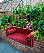 THE WALLED GARDEN AT COWDRAY  WEST SUSSEX. DESIGNER: JAN HOWARD - INSIDE THE CONSERVATORY/GREENHOUSE WITH RAISED BRICK BORDER WITH BANANA PLANTS AND RED SOFA