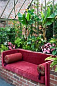 THE WALLED GARDEN AT COWDRAY  WEST SUSSEX. DESIGNER: JAN HOWARD - INSIDE THE CONSERVATORY/GREENHOUSE WITH BANANA PLANTS IN RAISED BRICK BORDER AND RED SOFA
