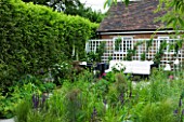 DESIGN: CHARLOTTE ROWE  LONDON. SMALL SECLUDED COUNTRY GARDEN IN JUNE WITH SOFA  TRELLIS  DIGITALIS PURPUREA ALBA (WHITE FOXGLOVES) AND PERENNIALS WITH GLASS LANTERNS