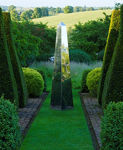 DAVID_HARBER_SUNDIALS_STAINLESS_STEEL_OBELISK_SUNDIAL_ON_GRASS_PATH_WITH_YEW_TOPIARY__AT_PETTIFERS__