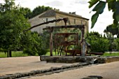 LA NORIA  FRANCE. GARDEN DESIGNED BY ARNAUD MAURIERES AND ERIC OSSART - NORIA - WATER PUMP WITH FARMHOUSE IN THE BACKGROUND