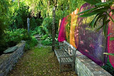 JARDIN_DES_SAMBUCS__FRANCE__THE_STONE_BRIDGE_WITH_MULTICOLOURED_CURTAINS_AND_WOODEN_BENCH