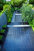 TANIA LAURIE  LONDON. OVERVIEW OF SMALL CONTEMPORARY GARDEN WITH PAINTED BLACK DECK LEADING TO TABLE AND GREY POLISHED PEBBLED PATIO. ON THE RIGHT ARE CATALPA.