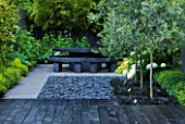 TANIA LAURIE  LONDON. SMALL CONTEMPORARY GARDEN BY CHARLOTTE ROWE. BLACK DECK WITH GREY POLISHED PEBBLES AND CATALPA SET INTO SQUARES PLANTED WITH OPHIOPOGON. BLACK MARBLE TABLE