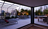 CONTEMPORARY FORMAL ROOF TERRACE/ GARDEN DESIGNED BY DATA NATURE ASSOCIATES: VIEW OUT OF APARTMENT TO SEATING AREA  BARBEQUE  SUN LOUNGERS AND CUSHIONS AT NIGHT. LIGHTING
