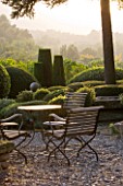 PROVENCE  FRANCE: GARDEN OF NICOLE DE VESIAN  LA LOUVE: GRAVEL TERRACE BESIDE THE HOUSE AT DAWN WITH METAL TABLE AND CHAIRS AND CLIPPED TOPIARY SHAPES