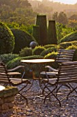 PROVENCE  FRANCE: GARDEN OF NICOLE DE VESIAN  LA LOUVE: GRAVEL TERRACE BESIDE THE HOUSE AT DAWN WITH METAL TABLE AND CHAIRS AND CLIPPED TOPIARY SHAPES