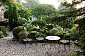 PROVENCE  FRANCE: GARDEN OF NICOLE DE VESIAN  LA LOUVE: GRAVEL TERRACE AT DAWN WITH METAL TABLE AND CHAIRS AND CLIPPED TOPIARY SHAPES