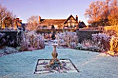 WOLLERTON OLD HALL  SHROPSHIRE: WINTER GARDEN IN FROST -  VIEW OF THE HOUSE WITH STONE SUNDIAL AND GRASS AREA IN FROST - DAWN LIGHT