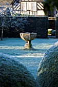 WOLLERTON OLD HALL  SHROPSHIRE: WINTER GARDEN IN FROST -  THE FONT GARDEN WITH A LIMESTONE FONT SEEN THROUGH LARGE BOX TOPIARY BALLS WITH HOUSE BEHIND
