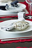 CHRISTMAS TABLE SETTING - NAPKIN AND SILVER BAUBLE DECORATION ON A WHITE PLATE. SARAH EASTEL LOCATIONS/ DI ABLEWHITE