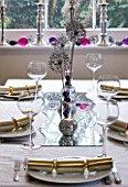 CLARE MATTHEWS CHRISTMAS HOUSE INTERIOR: THE KITCHEN WITH TABLE LAID FOR CHRISTMAS - PLATES WITH CRACKERS  CANDLES ON MIRROR  WINE GLASSES  BAUBLES  DRIED ALLIUMS