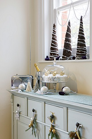 CLARE_MATTHEWS_CHRISTMAS_HOUSE_INTERIOR_WINDOWSILL_DECORATED_WITH_SILVER_CANDLES__BAUBLES_AND_SILVER