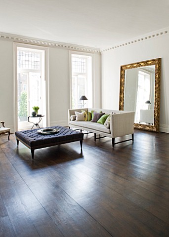 DESIGNER_JOHN_MINSHAW__THE_SITTING_ROOM_WITH_WOODEN_FLOOR__SETTEE__CUSHIONS_AND_MASSIVE_MIRROR_BESID