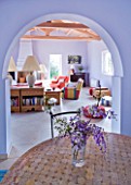DESIGNER GINA PRICE - CORFU - VILLA ONEIRO - VIEW FROM DINING AREA WITH TABLE AND JUG WITH WISTERIA AND BLOSSOM TO LARGE LIVING ROOM BEYOND