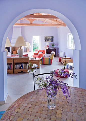 DESIGNER_GINA_PRICE__CORFU__VILLA_ONEIRO__VIEW_FROM_DINING_AREA_WITH_TABLE_AND_JUG_WITH_WISTERIA_AND