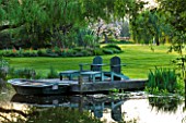 ULTING WICK  ESSEX: SPRING - A PLACE TO SIT - DECKED TERRACE BESIDE THE LAKE WITH ADIRONDACK WOODEN CHAIRS/ SEATS AND BOAT