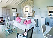 DESIGNER: CLAIRE SKINNER  ROU ESTATE  CORFU: HOUSE 11 (LAVENDULA) INTERIOR - LIVING ROOM IN GREY  CREAM AND PINK. GLASS COFFEE TABLE  SOFA WITH CUSHIONS  IRIS IN VASE